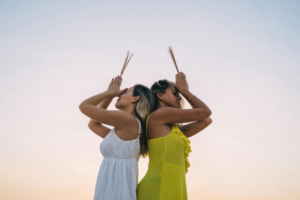 Women practicing meditation with incense sticks outdoors during sunset, reflecting tranquility.